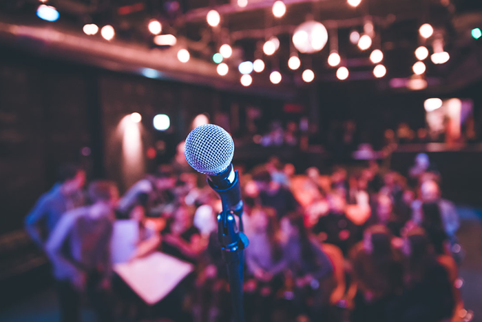 Close up of single microphone on stage in front of out of focus crowd.